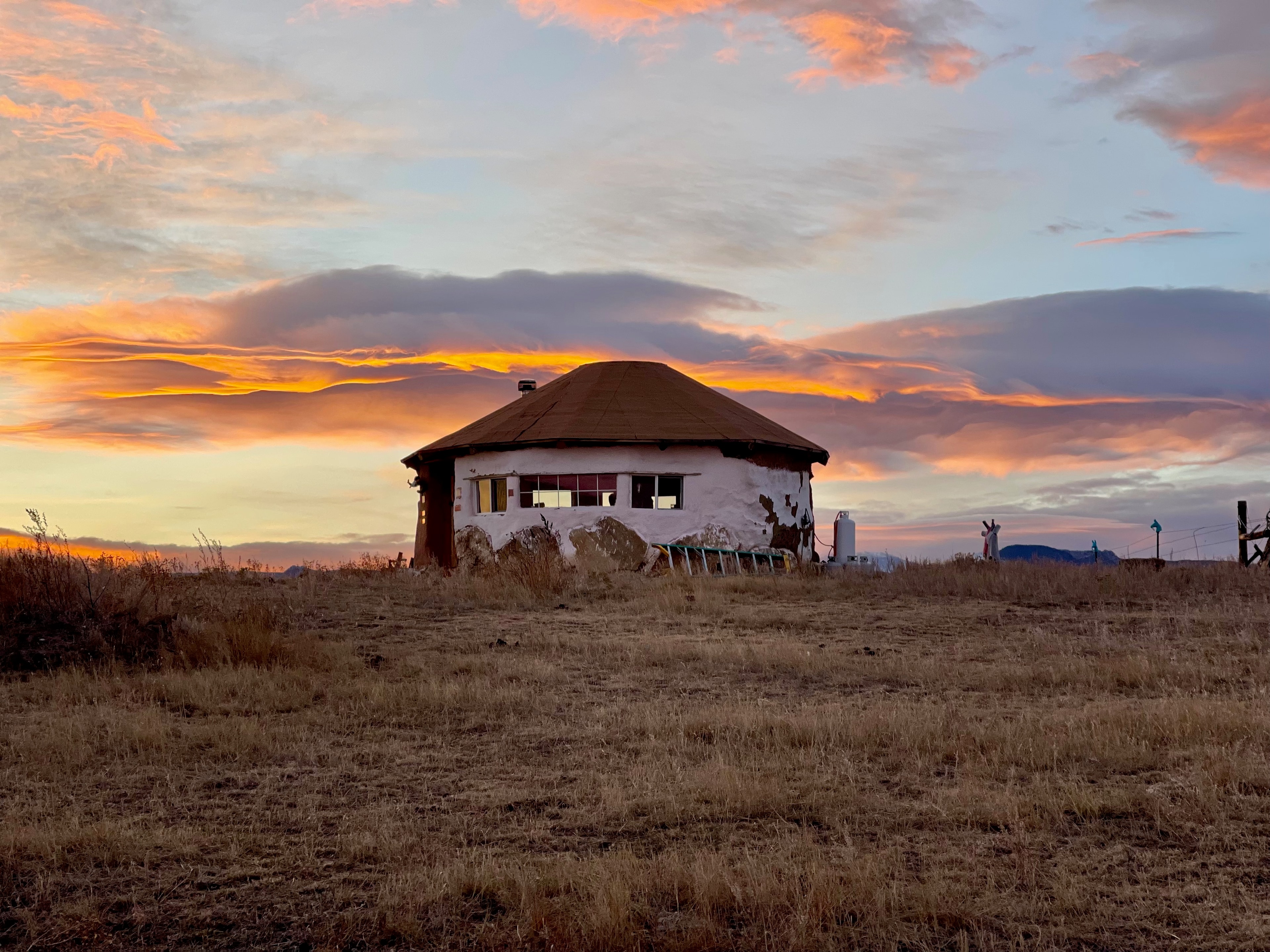 A rustic round ranch building in an open field beneath a colorful sunset